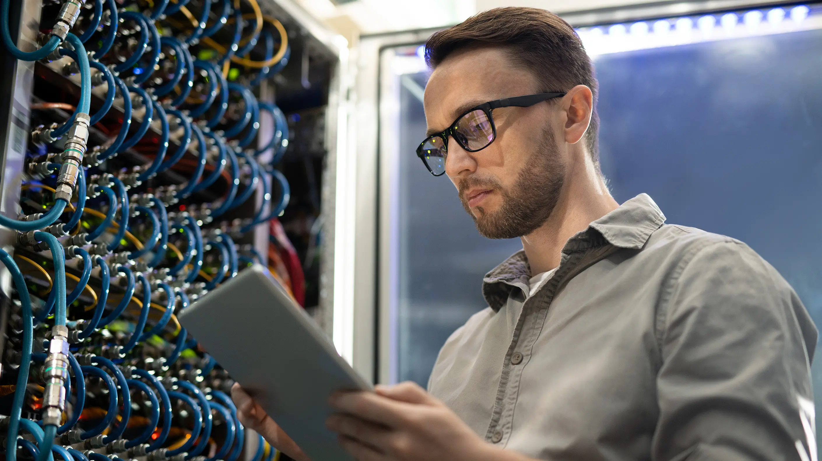 Network manager looking at a tablet while working on a server room's connections.