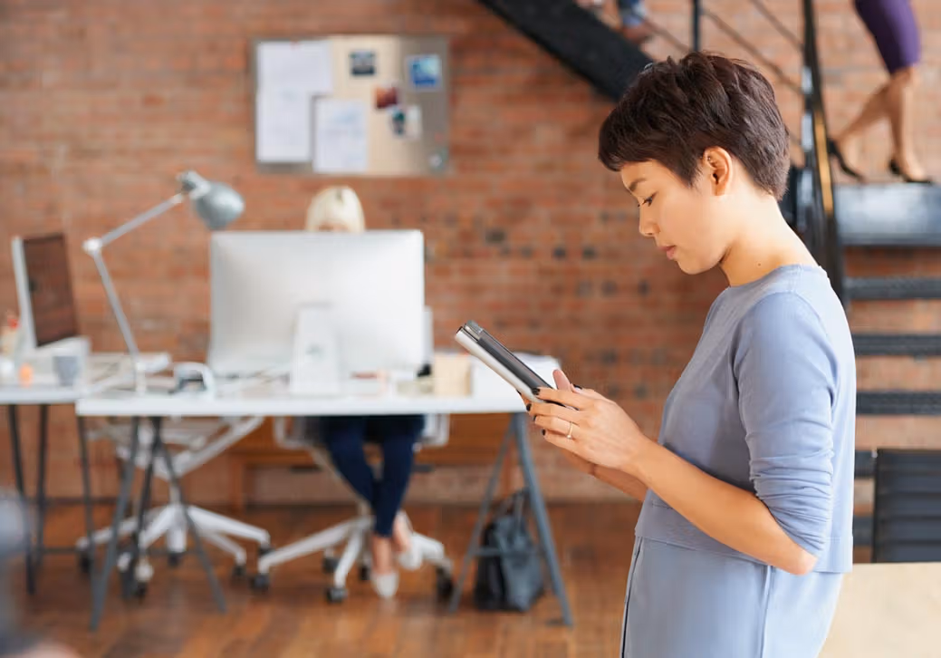 A kid using a tablet while their parent works from home in the background.