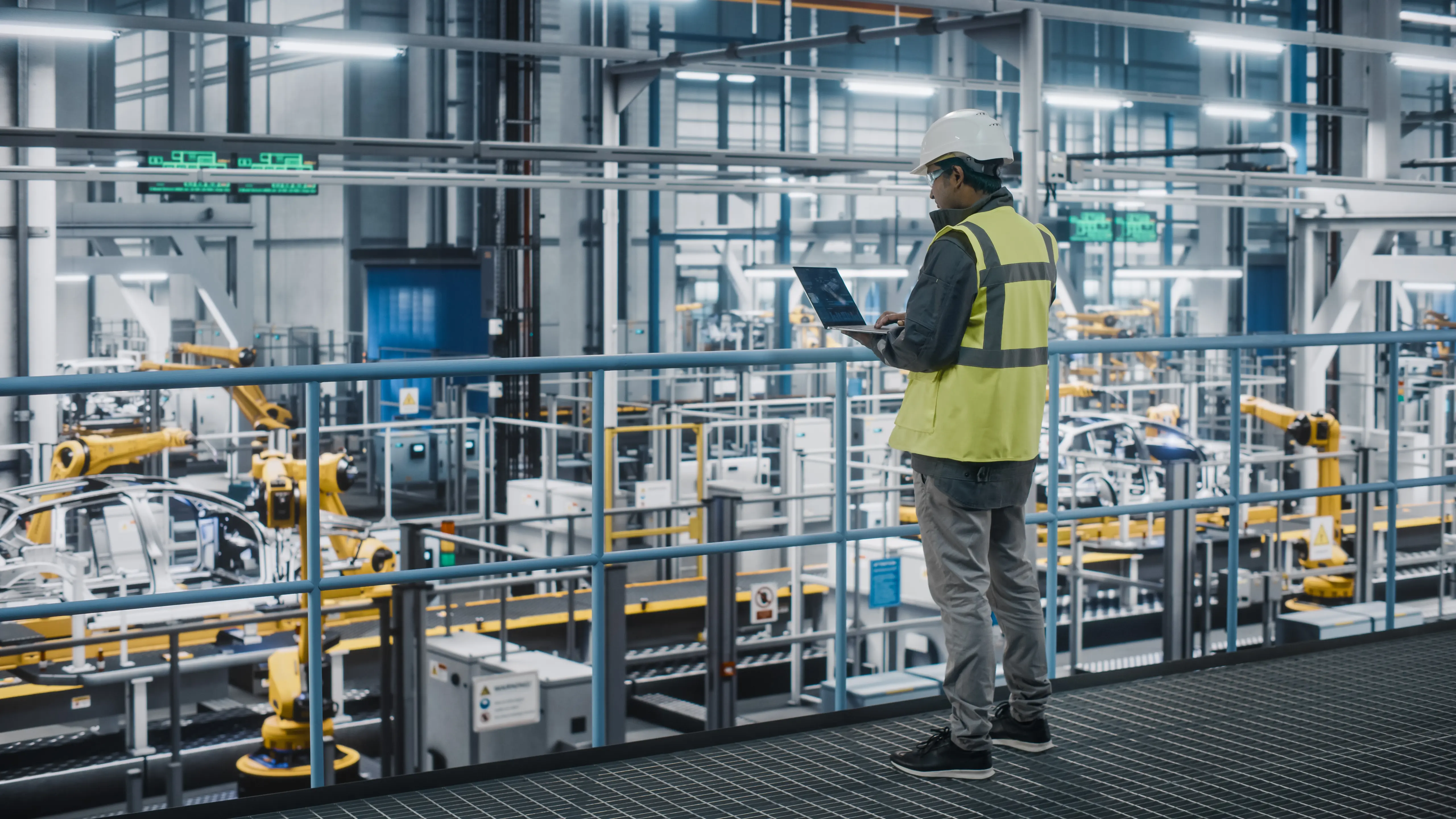 Man in factory worker attire looking over IIoT machines connected via data transmission lines and 5G.