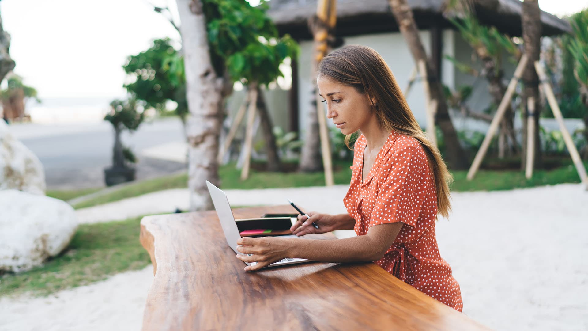 A digital nomad working from out of office on a wooden table at a beach.