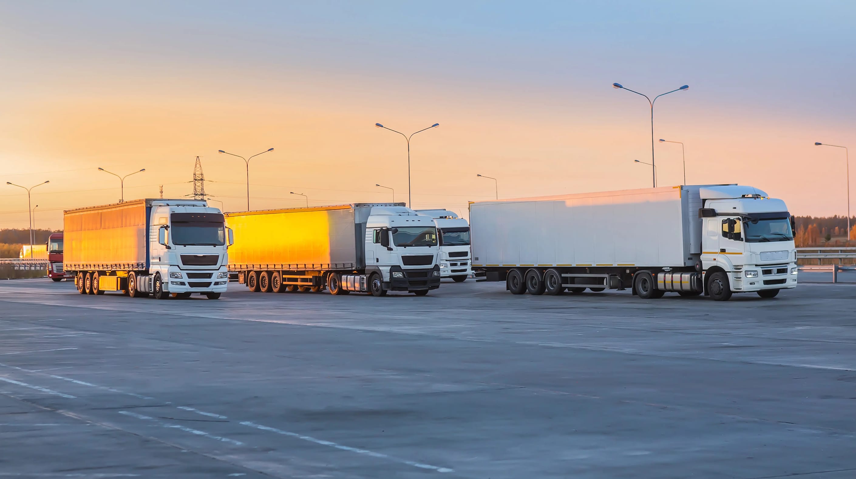 Four trucks all idling in a parking lot as the sun sets in the background.