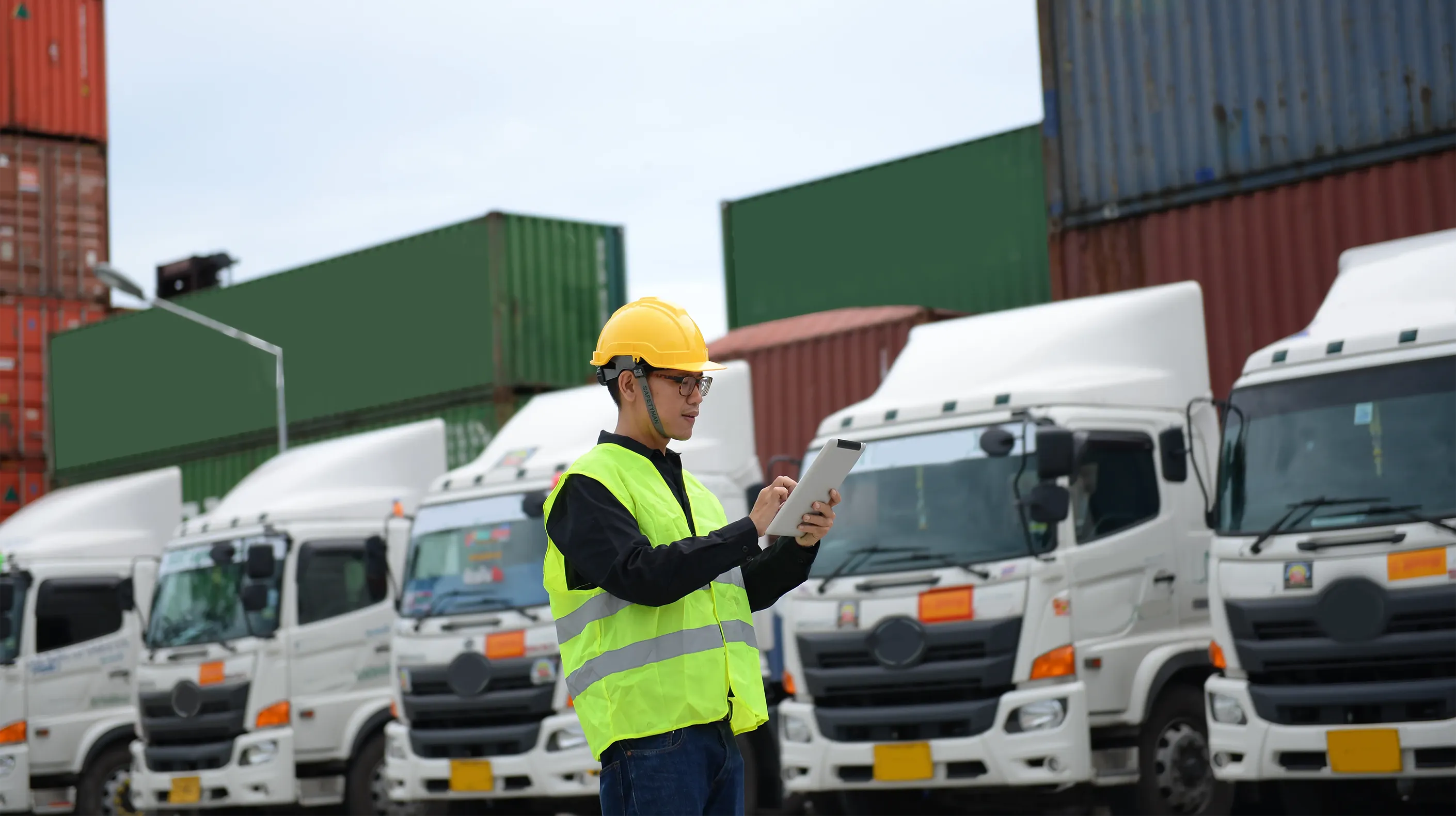 Fleet manager looking at a tablet while standing in front of a few trucks and cargo boxes.